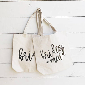 Sturdy medium size natural color bride and bridesmaid canvas tote bag for bridal party on white wooden background.