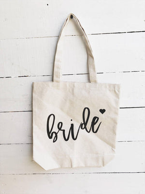 Sturdy natural color canvas tote for bridesmaid on white wooden backdrop.