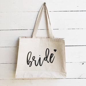 Sturdy large natural color bride canvas tote bag for bridal party on white wooden background.
